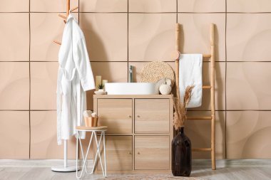 Bornozlu, lavabolu ve ahşap dolaplı banyo aksesuarları.