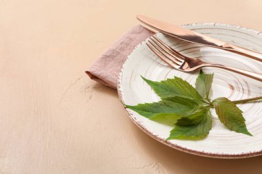 Temiz tabak, çatal bıçak ve yeşil bitki yapraklarıyla bej arka planda güzel bir masa.