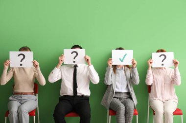 Genç başvuranlar, ellerinde kontrol kağıtları ve odada soru işaretleri olan kağıtlar tutuyorlar