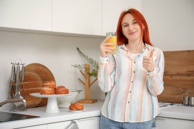 Mutfakta bir bardak meyve suyu içen genç kızıl saçlı kadın.