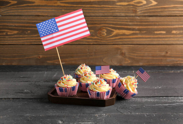 Tray tasty patriotic cupcakes with flags of USA on black table near brown wooden wall. American Independence Day