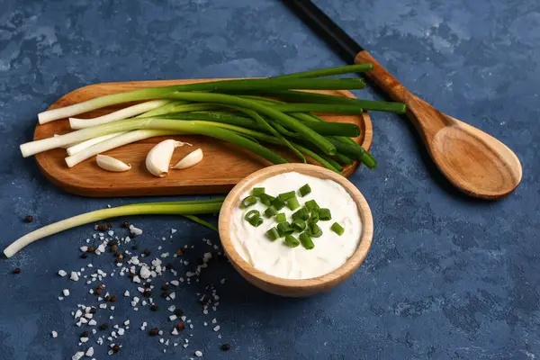 Bir kase lezzetli ekşi krema ve yanında yeşil soğanlı mavi arka plan.