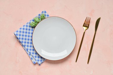 Boş tabak, çatal bıçak, hoplama ve pembe masanın üzerindeki mavi kareli peçete.