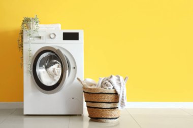 Sarı duvarın yanında kirli çamaşır ve çamaşır makinesi olan bir sepet.