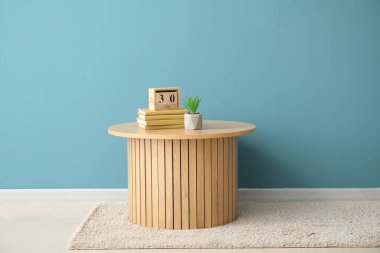 Kitaplı kahve masası, küp takvimi ve mavi duvarın yanındaki bitki örtüsü.