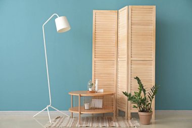 Dekorlu kahve masası, ev bitkisi ve mavi duvarın yanındaki katlanır ekran.