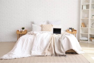 Beyaz battaniyeli dağınık yatak odası ve modern laptop.