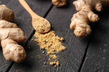 Taze zencefil kökleri ve siyah ahşap arka planda kurutulmuş toz ile kaşık.