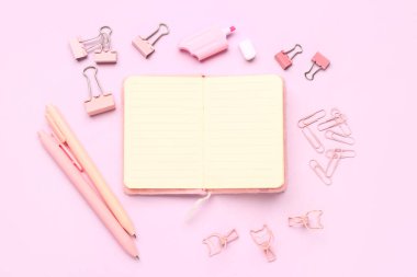 Pembe arka planda farklı kırtasiye malzemesi içeren defter.