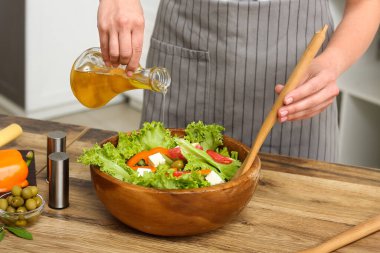 Mutfaktaki masada lezzetli salata ile zeytinyağı ekleyen bir kadın.