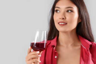 Gri arka planda bir bardak şarabı olan güzel bir Asyalı kadın.