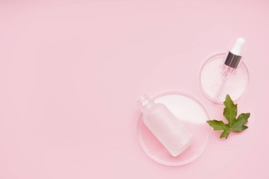 Pembe arka planda bitkilerle ve bir şişe kozmetik ürünlerle dolu petri kapları.