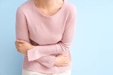 Mavi arka planda karın ağrısı çeken genç bir kadın, yakın plan.