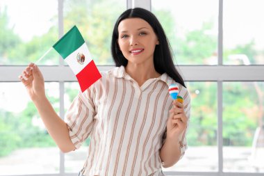 Evinin penceresinin yanında Meksika bayrağı ve marakas taşıyan genç bir kadın.