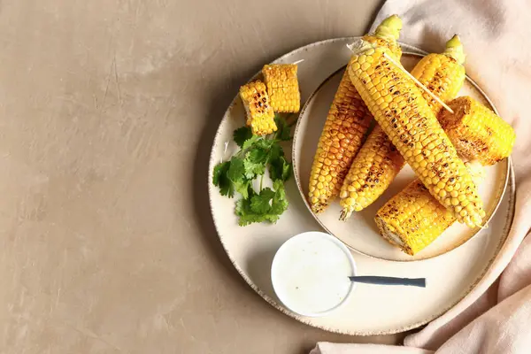 Lezzetli ızgara mısır koçanı ve kahverengi arka planda sos tabağı.