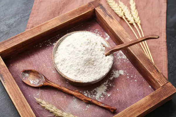 Kaseli ahşap tepsi, buğday unu ve siyah grunge arka planda kaşık.