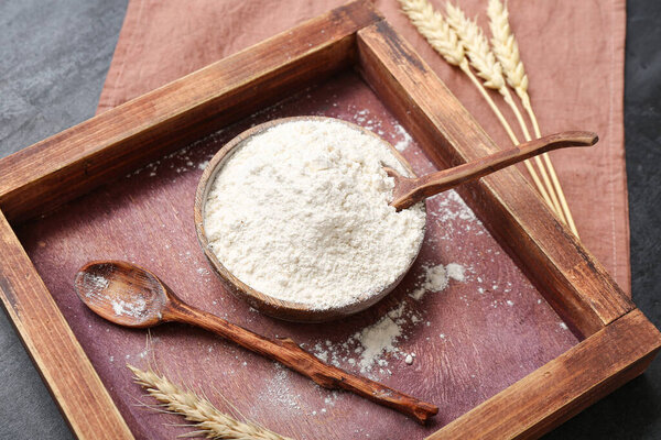 Деревянный поднос с миской, пшеничной мукой и ложкой на черном фоне гранжа
