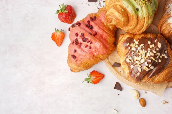 Farklı tatlı kruvasanları ve beyaz arka planda çilekleri olan ahşap bir tahta tahta.