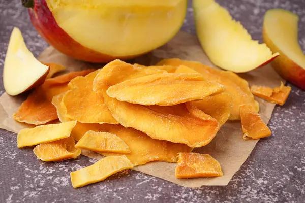 Koyu masa üzerinde kurutulmuş mango dilimleri olan kağıt fırını.