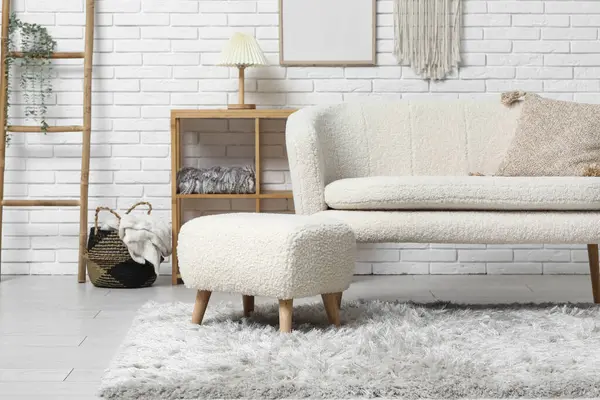 Beyaz tuğla duvarın yanında kanepe ve puf olan modern oturma odasının içinde.