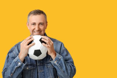 Sarı arka planda futbol topuyla oynayan yakışıklı olgun bir adam.