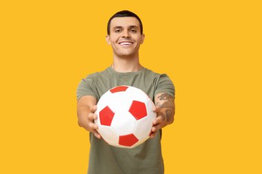 Sarı arka planda futbol topu olan yakışıklı genç adam.