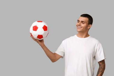 Gri arka planda futbol topu olan yakışıklı genç adam.