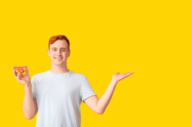 Genç adam elinde lezzetli bir pizza tutuyor ve sarı arka planda bir şeyler gösteriyor.
