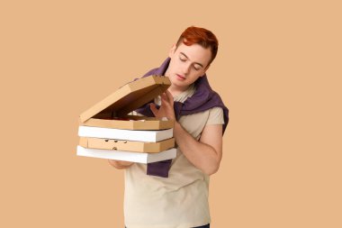 Elinde kahverengi arka planda lezzetli pizzalar olan karton kutular tutan genç adam.