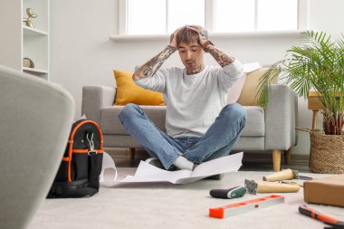 Stresli genç adam evde mobilya montajı yapıyor.