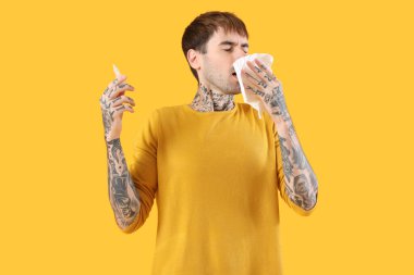 Sarı arka planda burun damlası ve dokuları olan alerjik genç bir adam.