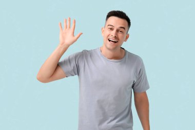 Yakışıklı adam mavi arka planda el sallıyor.