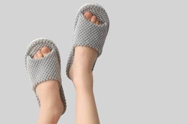 Gri arka planda yumuşak terlikler giymiş kadın bacakları.