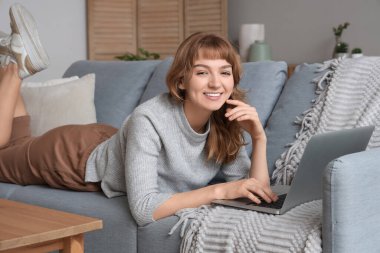 Dizüstü bilgisayarı olan genç bir kadın evdeki kanepede dinleniyor.