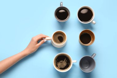 Mavi arka planda sıcak kahve fincanları olan bir kadın el.