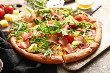 Tahta tahtada domatesli lezzetli pizza ve gri arka planda roka.