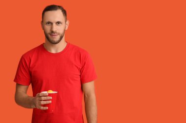 Turuncu arka planda plastik bardak soğuk birası olan genç adam.