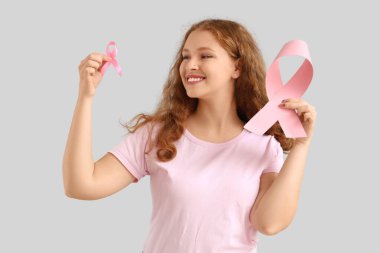 Açık arkaplanda pembe kurdeleli genç bir kızıl kadın. Göğüs kanseri farkındalığı konsepti