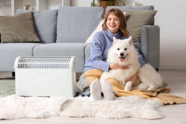 Ekoseli ve Samoylu köpekli genç bir kadın evdeki radyatörün yanında ısınıyor.