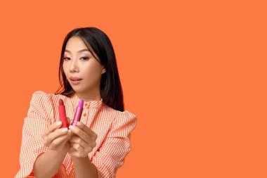 Turuncu arka planda farklı rujları olan güzel bir Asyalı kadın.