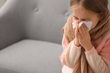 Evdeki kanepede hapşıran hasta küçük bir kız, yakın plan.