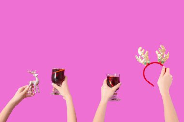 Sıcak şarap kadehleriyle kadın elleri ve pembe arka planda Noel dekoru.