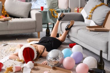 Sarhoş genç bir kadın yeni yıl partisinden sonra dağınık oturma odasında yerde yatıyor.