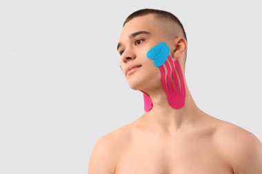 Yüzünde bant olan genç bir adam arka planda ışığa karşı, yakın plan