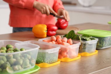 Sebzeli plastik kaplar ahşap masada donmak için kadınlar da arka planda.