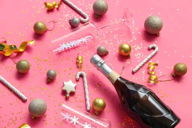 Gözlüklü bir şişe şampanya, baston şeker ve pembe arka planda Noel topları.