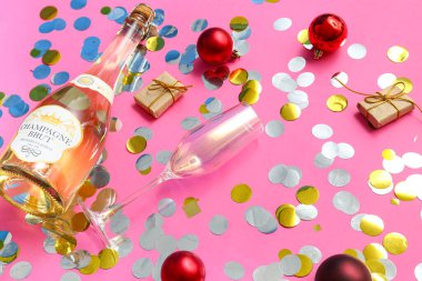 Bir şişe şampanya ve pembe arka planda Noel topları.