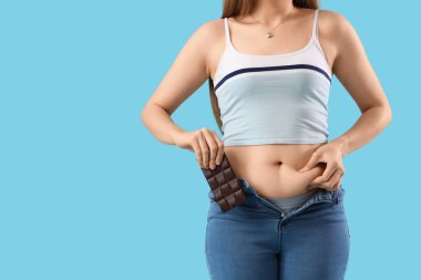 Dar kotlu, mavi arka planda çikolatalı genç bayan, yakın plan. Kilo alma kavramı