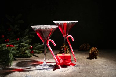 Bir bardak lezzetli kırmızı margarita, baston şekerler ve karanlık arka planda Noel dekoru.