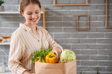 Mutfakta bir çanta dolusu sağlıklı yiyecekle genç bir kadın.